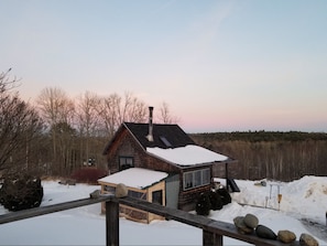 Cozy cabin with a prominent chimney and small porch area, surrounded by a snowy landscape.