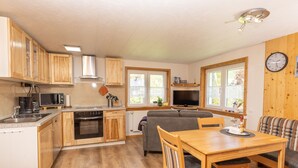 A compact kitchen with wooden cabinets, a microwave, stove, and a dining area with a table and chairs. - Very quiet holiday home in the Rothaar Mountains (Vormwald)