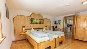 A wooden bed with pillows and a nightstand, a wooden wardrobe, and a kitchen area visible through an open door. - Very quiet holiday home in the Rothaar Mountains (Vormwald)