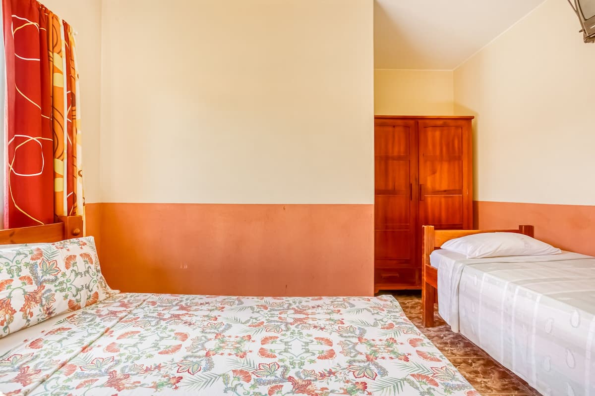 A bedroom with two beds, a wooden wardrobe, and a door leading to another room.