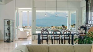 Amplia sala de estar con un gran ventanal que ofrece vistas a una montaña y al paisaje urbano. Hay un comedor con sillas de madera y una mesa, y un sofá en primer plano.