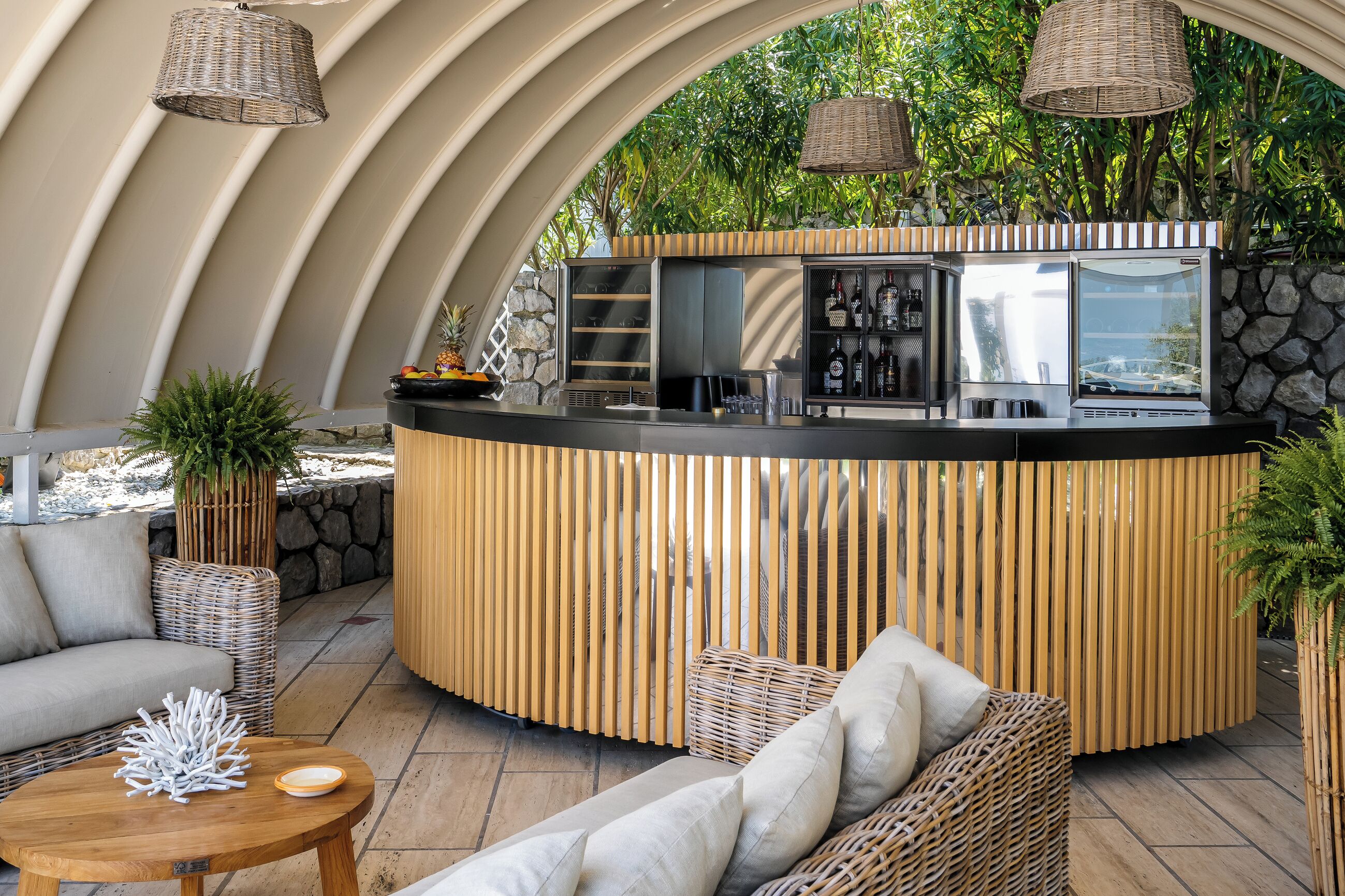 Eine gebogene Bar mit rustikaler Steinwand, Korbmöbeln und hängenden Lampen aus Weidwerk.