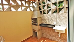 A compact kitchen with a built-in oven, a sink, and a window with a decorative grid. - Residencial Miragem Bombinhas Duo (Bombinhas)