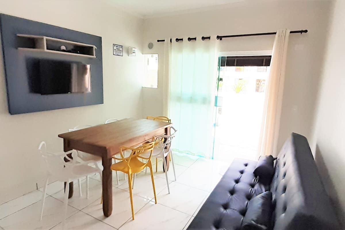 Un coin repas avec une table et des chaises en bois, un canapé noir et une étagère fixée au mur.