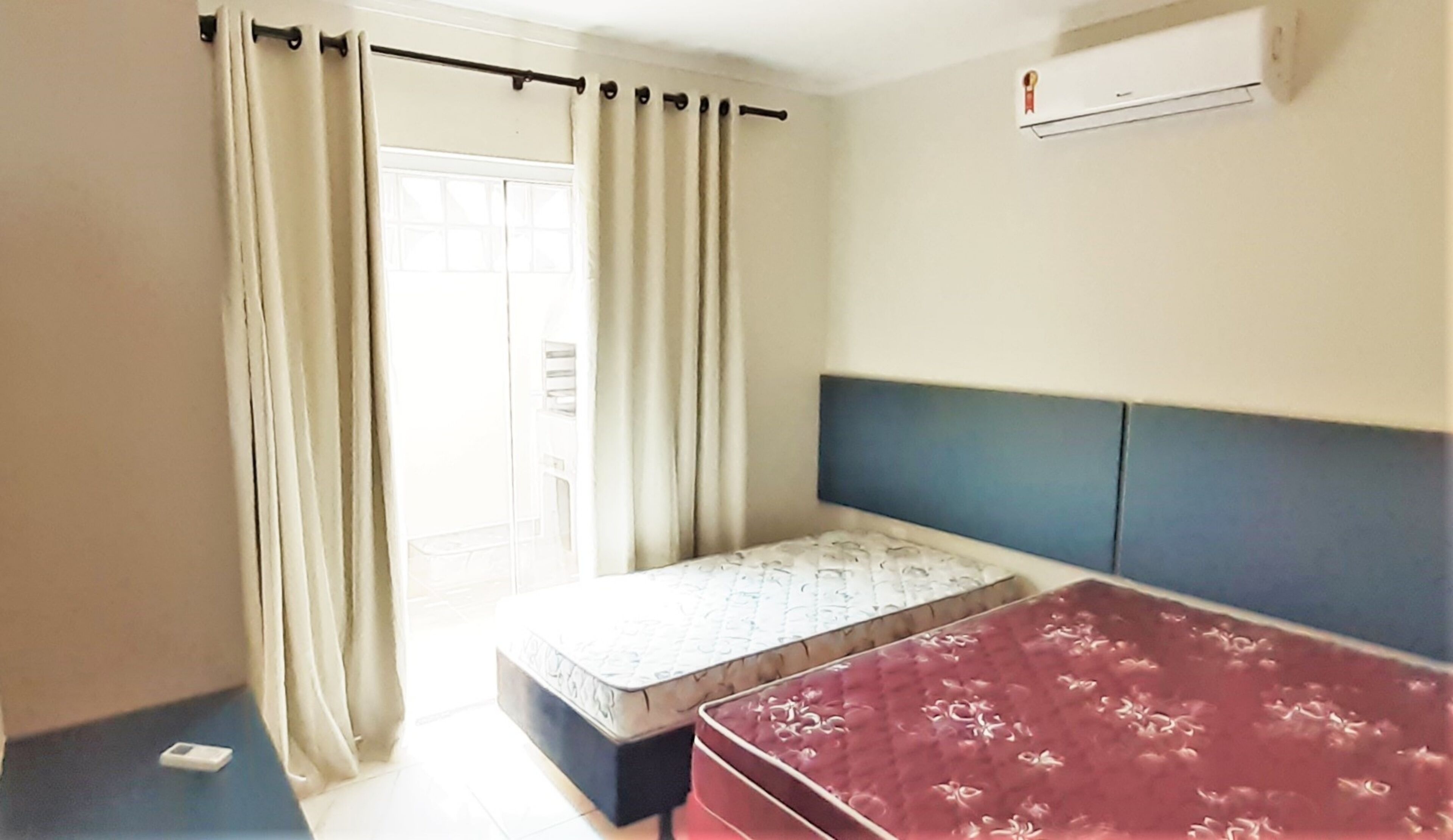 Una habitación pequeña con cama individual, cabecera, ventana con cortinas, colchón y mesita de noche.