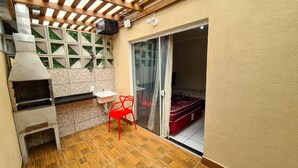 A compact kitchen with a built-in oven, a small sink, and a red chair. - Residencial Miragem Bombinhas Duo (Bombinhas)