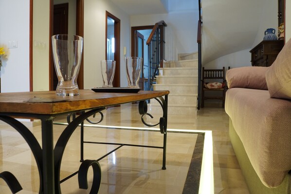 A living room with a wooden coffee table, two clear glass vases, a staircase, and a cushioned sofa. - Duplex Centro Parking Ronda (Ronda)
