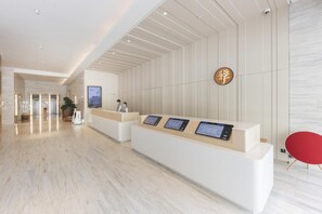 Ein Hotel-Empfangsbereich mit modernem Design, inklusive einer Rezeption, einem digitalen Bildschirm und einem roten Stuhl.