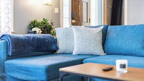 Ein blaues Sofa mit einer Decke, ein kleiner Tisch mit einer Fernbedienung und eine Wand mit Spiegel und Lampen.