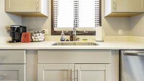 A kitchen with a stainless steel sink, a coffee maker, a red appliance, and a window with blinds. - Secluded, Cozy 4BR, A2 Old West Side (Ann Arbor)