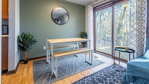 A modern living room with a wooden bench, a round mirror, and a large window with a view of trees. - Secluded, Cozy 4BR, A2 Old West Side (Ann Arbor)