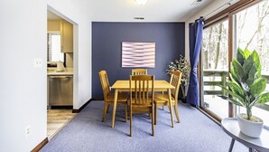 A dining area with a wooden table and chairs, a blue carpet, a ceiling light, and a window with curtains. - Secluded, Cozy 4BR, A2 Old West Side (Ann Arbor)