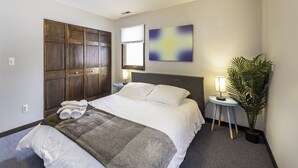 A hotel room with a large bed, a wooden wardrobe, a small table with a lamp, a potted plant, and a painting on the wall. - Secluded, Cozy 4BR, A2 Old West Side (Ann Arbor)