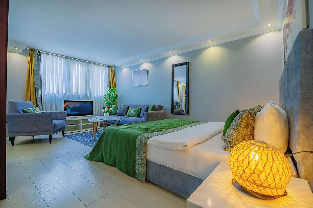 A modern hotel room with a bed, a sofa, a TV, and a lamp.