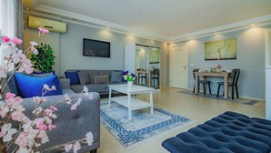 Ein modernes Wohnzimmer mit einem grauen Sofa, blauen Kissen, einem weißen Couchtisch und einem blau gemusterten Teppich.