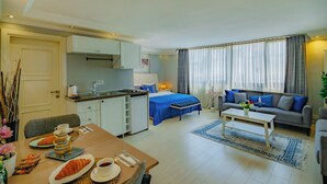 Ein modernes Hotelzimmer mit Essbereich, einer Küchenzeile und einer Wohnbereitschaft mit Sofa und großem Fenster.