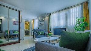 Ein modernes Wohnzimmer mit Sofa, Couchtisch und Fernseher. Es gibt einen Essbereich mit Tisch und Stühlen. Ein großes Spiegelbild zeigt einen Teil des Raumes.
