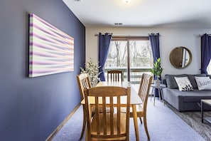 A dining area with a table and chairs, a sofa with cushions, a potted plant, and a large abstract painting on the wall.
