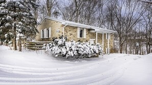 A two-story house with a brick exterior and white shutters, surrounded by snow-covered trees and a snow-covered lawn. - Secluded 2BR Loft - Minutes from Downtown AA! (Ann Arbor)
