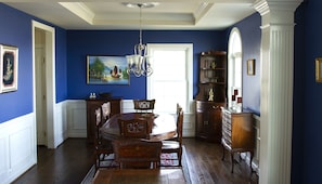 A dining room with a wooden table and chairs, a chandelier, and a large painting on the wall.