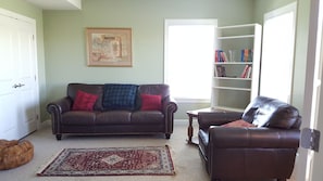 A living room with a brown leather sofa, a matching armchair, a coffee table, a bookshelf, and a patterned rug.