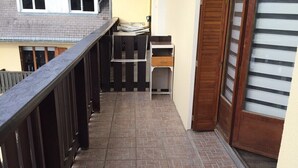 A balcony with a wooden railing, a small table with a chair, and a door with a striped pattern. - C - Refurbished accommodation / sleeps 4 (Lans-en-Vercors)