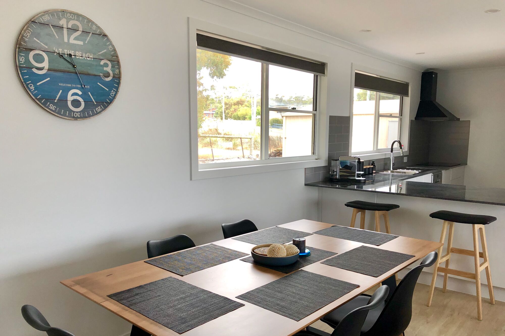 A modern kitchen with a large island, a dining area with a wooden table and chairs, and a wall-mounted clock.