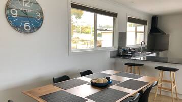 A modern kitchen with a large island, a dining area with a wooden table and chairs, and a wall-mounted clock.