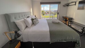Ein Schlafzimmer mit Bett, Nachttisch, Lampe und Blick ins Freie.