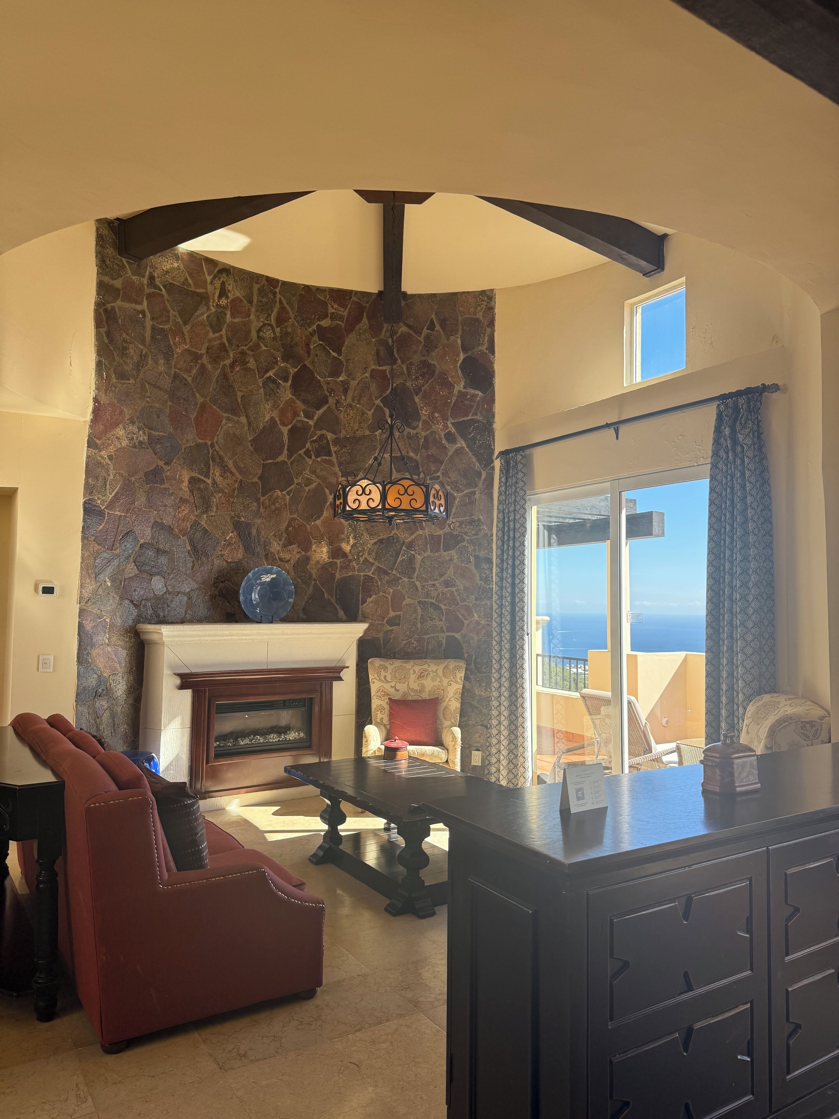 A living room with a stone wall, a fireplace, a red sofa, a dining table, and a view of the ocean.