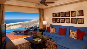 A living room with a blue sofa, a coffee table, and a TV. There are framed pictures on the wall and a view of the ocean. - Luxury villa in Cabo San Lucas (Cabo San Lucas)