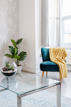 A teal armchair with a yellow striped throw blanket, a potted plant, and a glass-top coffee table with a decorative bowl. - ☆LUXURY APARTMENT☆BUSINESS/RELOCATIONS☆2BED (Ilford)