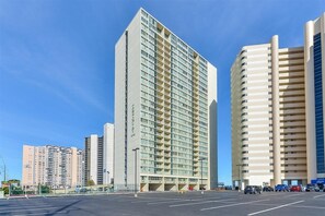 Un hotel de gran altura con varios pisos, un estacionamiento al frente y otros edificios al fondo.
