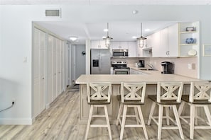 Una cocina moderna con armarios blancos, una isla grande con taburetes de bar, electrodomésticos de acero inoxidable e iluminación colgante.