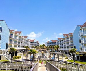 A beachfront hotel with multiple-story buildings, balconies, and a central walkway.