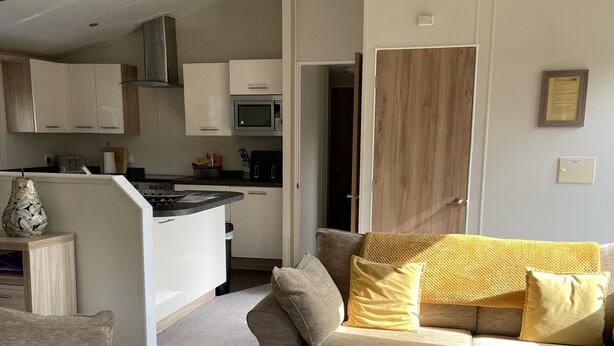 A modern living room with a grey sofa, a coffee table, and a kitchen in the background.