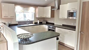 A modern kitchen with white cabinets, a stainless steel range hood, a microwave, and a built-in oven. - Little Fawn Felmoor Park (Morpeth)