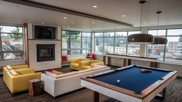 A modern indoor pool area with a pool table, yellow sofas, and large windows offering city views. - Domicile Suites at Venn on Main (Bellevue)