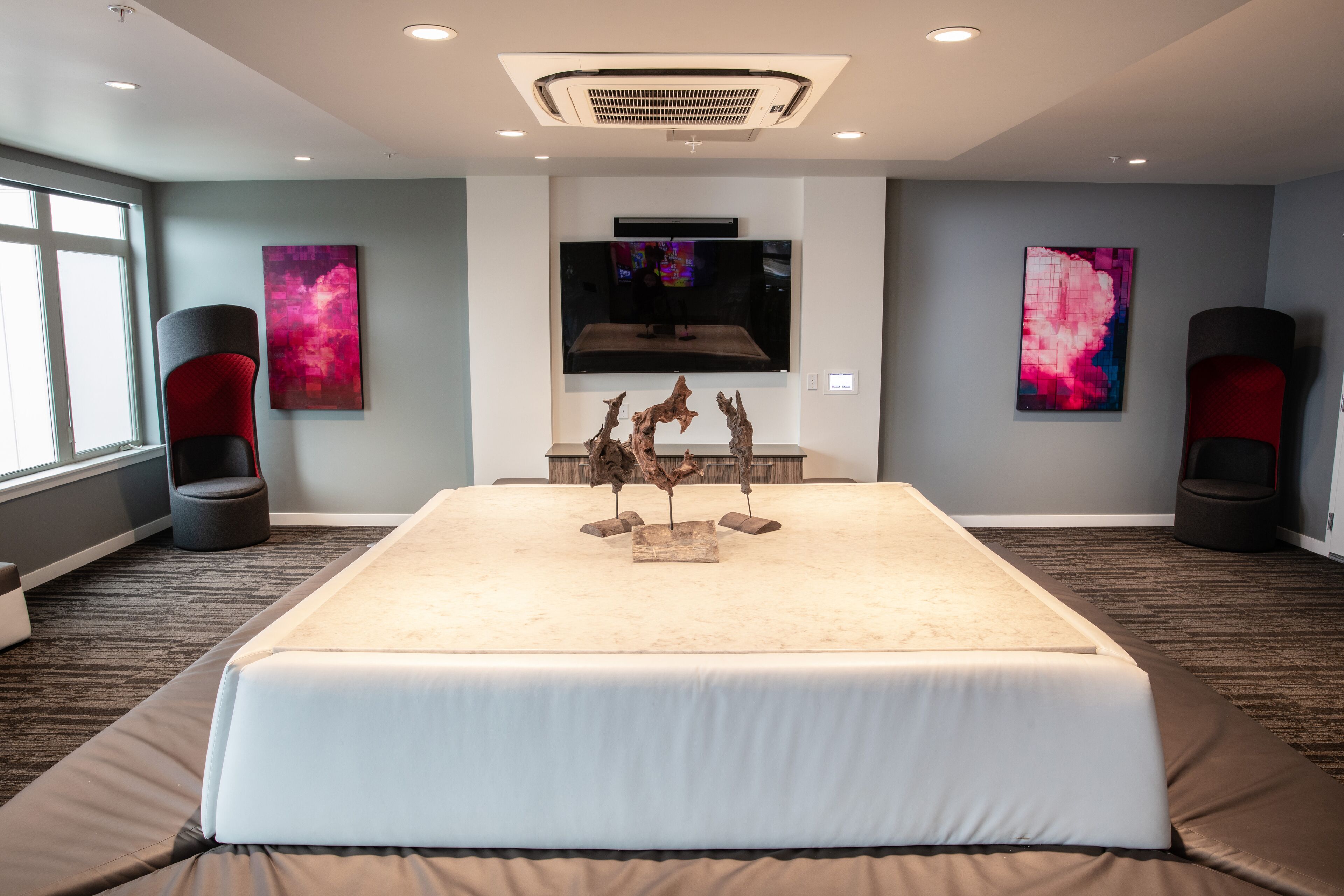 A hotel room with a large bed, a mounted TV, and abstract art on the walls.