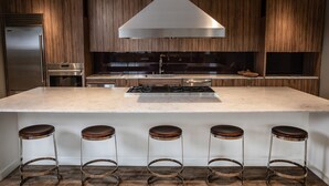 A modern kitchen with a large island, stainless steel appliances, and wooden cabinetry. - Domicile Suites at Venn on Main (Bellevue)