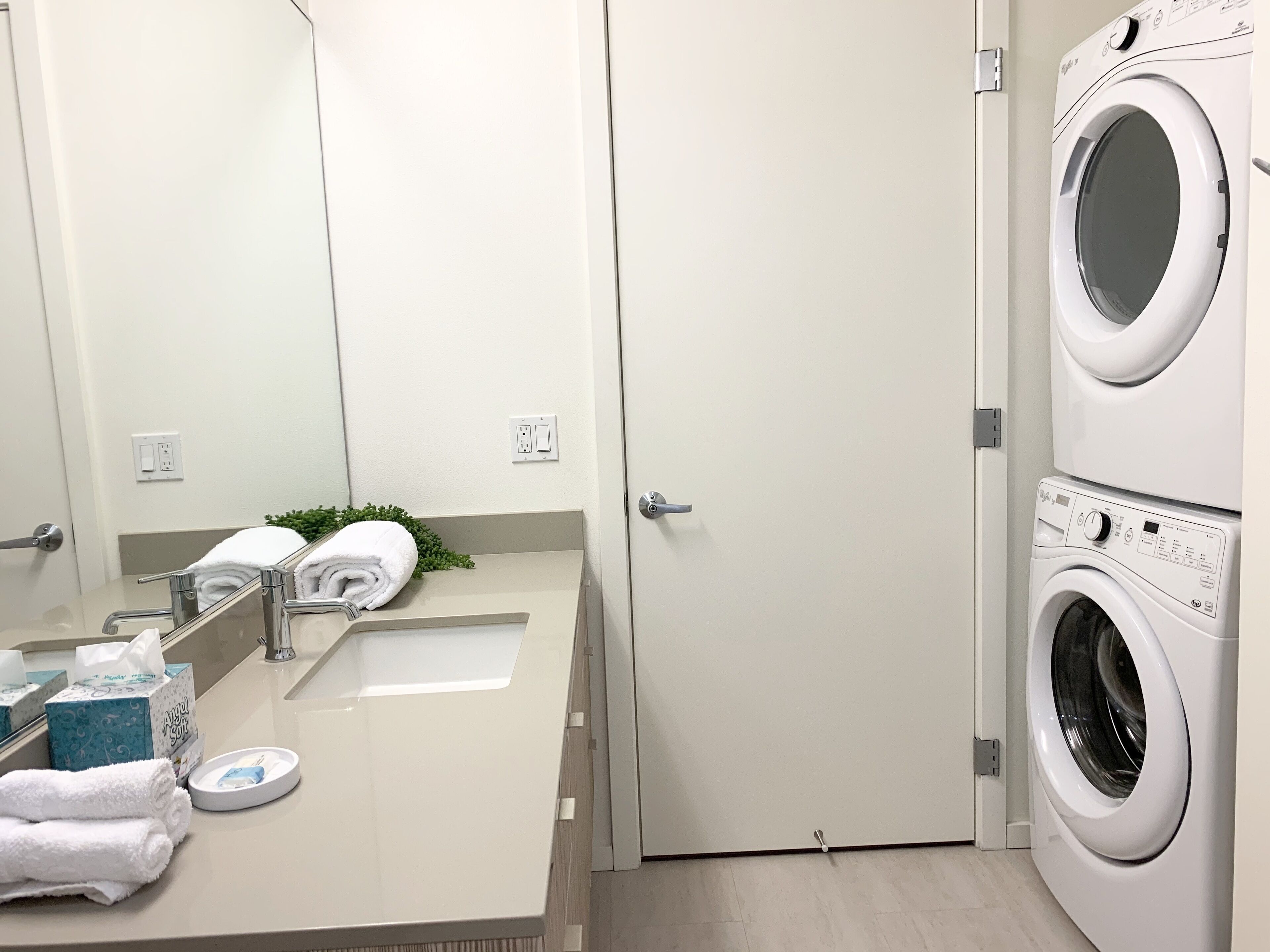 A hotel bathroom with a sink, mirror, towel rack, and stacked towels.
