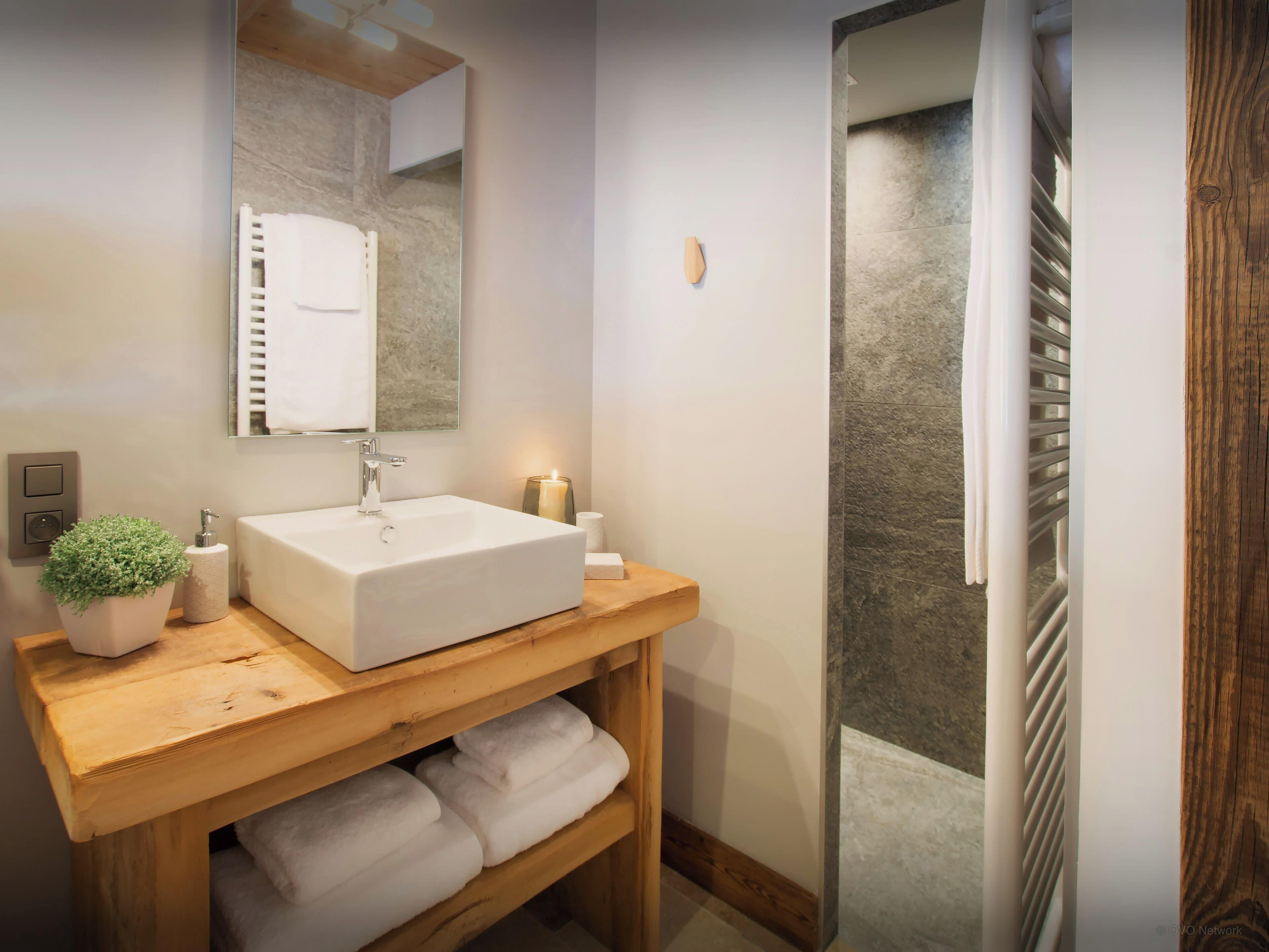Ein modernes Badezimmer mit einem weißen Waschbecken, einem Holz-Waschtisch und einer Duschkabine aus Glas.