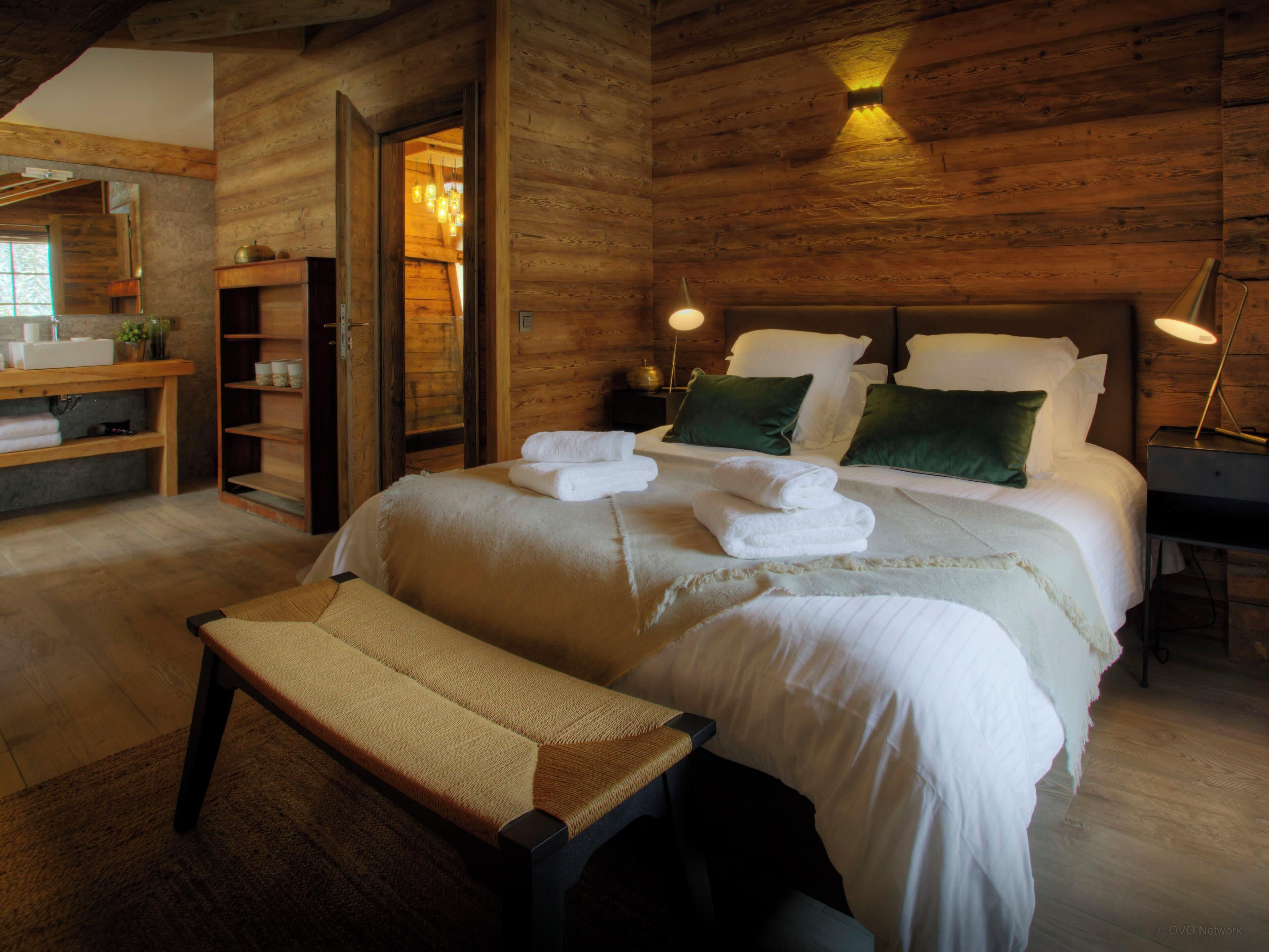 Ein Schlafzimmer mit Holzwänden, einem Bett, Nachttischlampen und einer Bank.