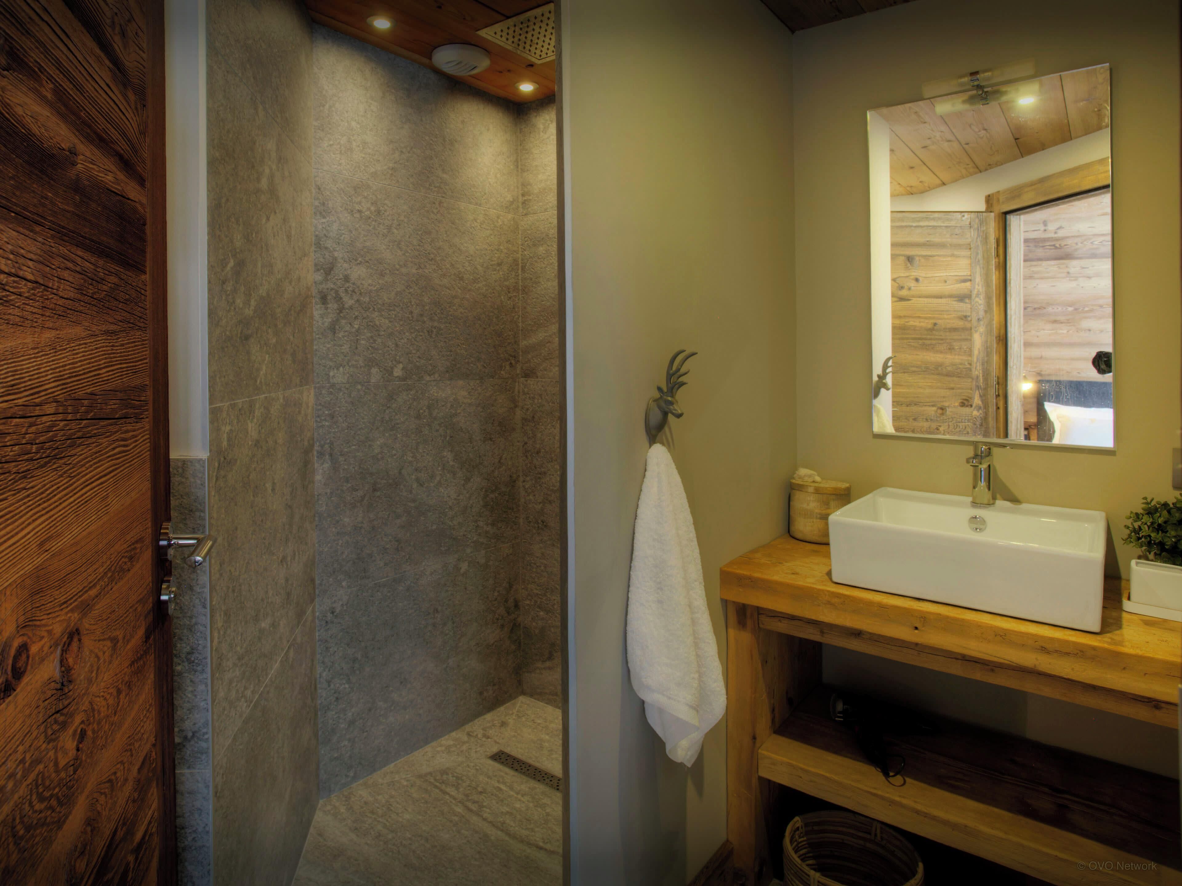 Une salle de bain avec une porte en bois, un espace de douche en pierre, un meuble-lavabo en bois avec un évier et un miroir.