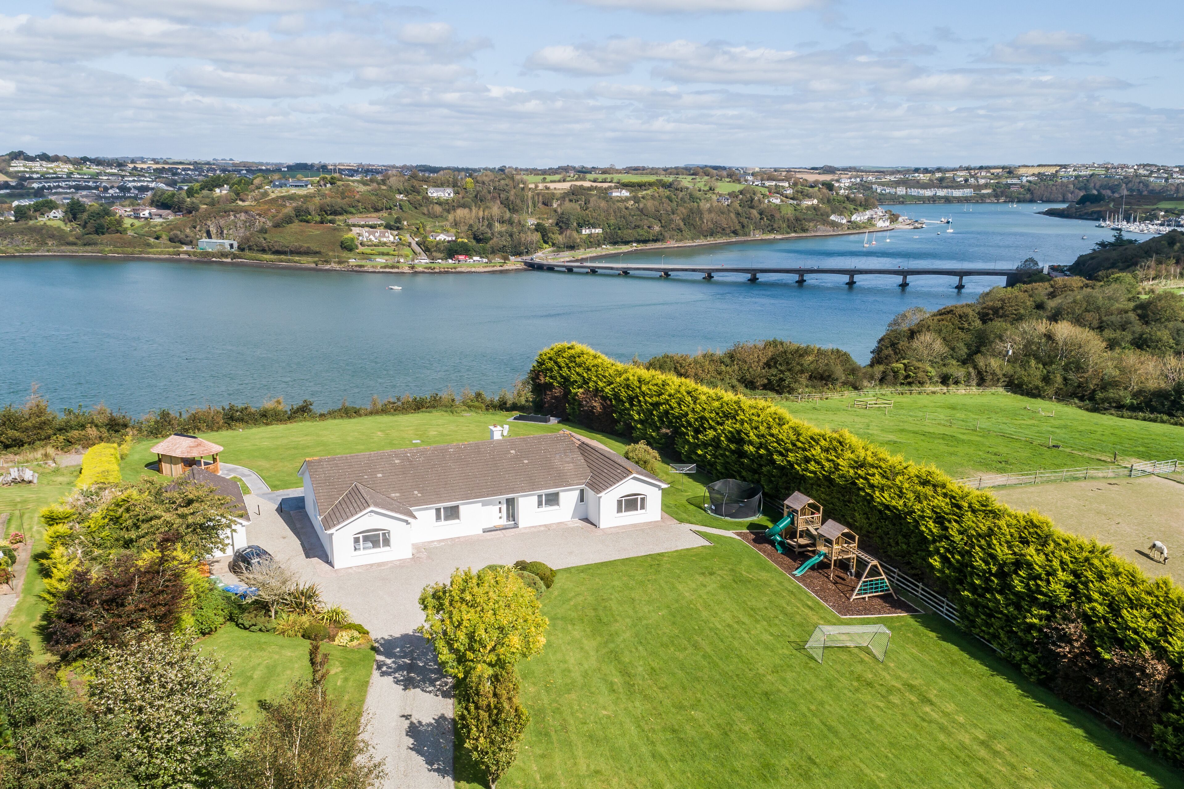 A house with a large lawn, a play area, and a view of a river with a bridge.