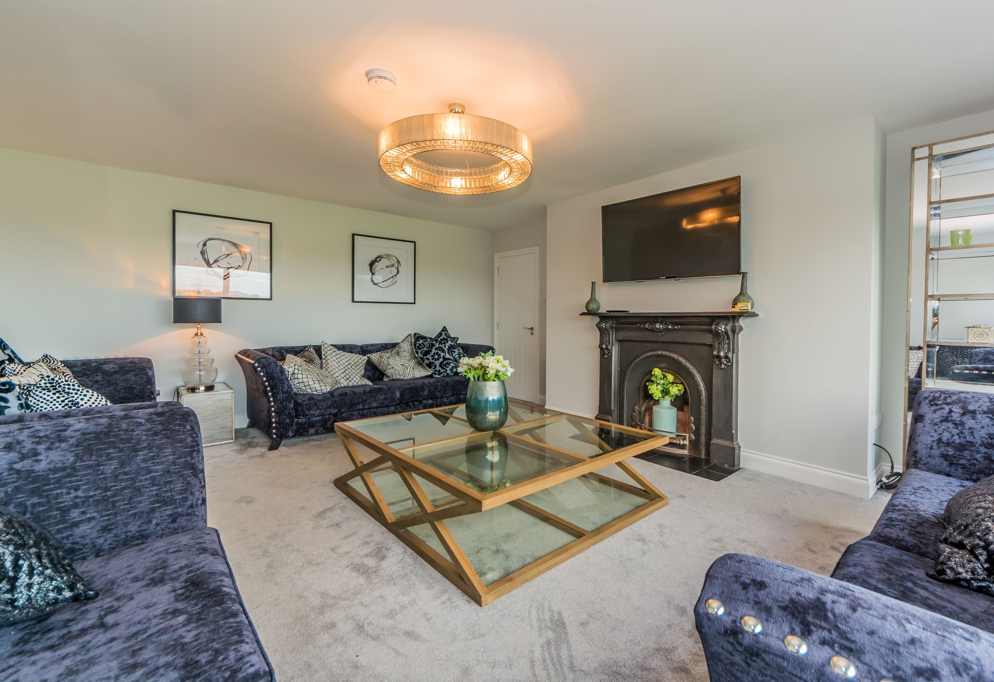 A living room with a glass-top coffee table, dark blue sofas, a fireplace, and a mounted TV.