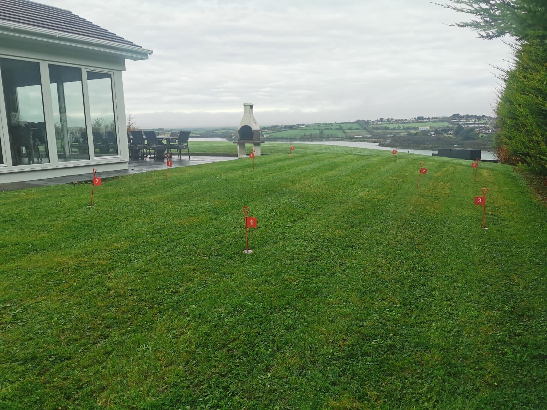 A grassy area with numbered markers, a building with large windows, and a distant view of a body of water and hills.
