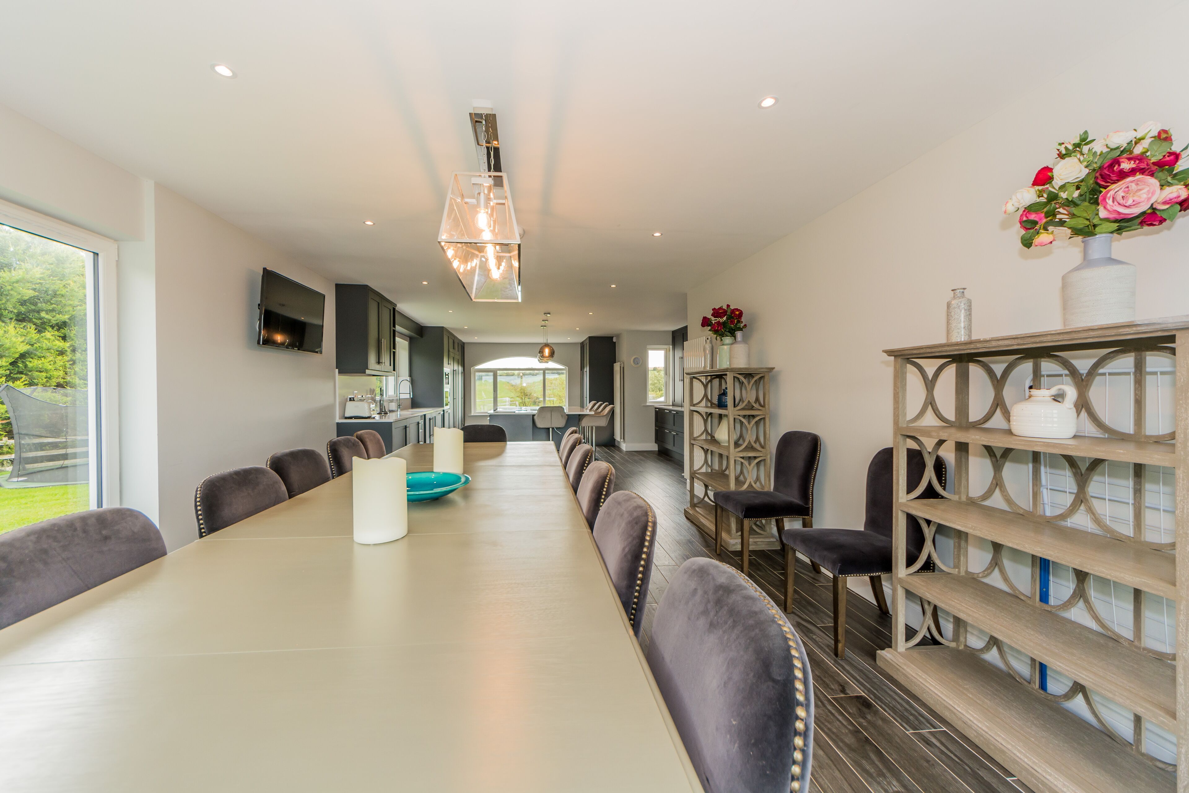 A modern kitchen with a long dining table, built-in seating, and a decorative shelf.