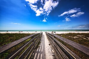 A beach with a wooden boardwalk leading to the shore, clear blue sky, and calm sea. - Luxurious Beach Front Condo with Spectacular Views! (Naples)