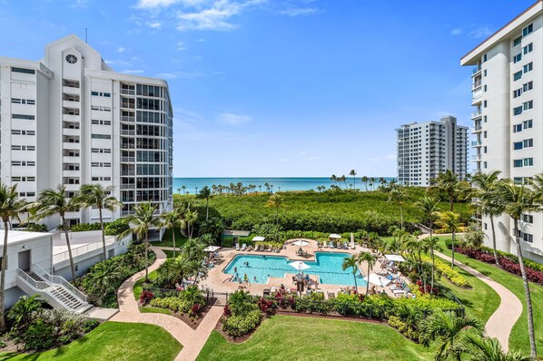 A resort with a pool, palm trees, and a view of the ocean. - Luxurious Beach Front Condo with Spectacular Views! (Naples)